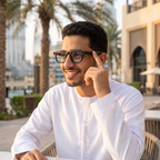 Man wearing AIMB-G1 AI smart glasses at an outdoor Dubai cafe